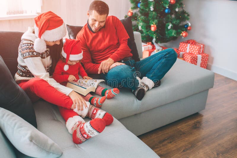 Feliz Navidad y Feliz Año Nuevo Familia que se sienta junto en el sofá La pequeña muchacha está entre sus padres Ella se sostiene fotografía de archivo Feliz Navidad y Feliz Año Nuevo Familia que se sienta junto en el sofá La pequeña muchacha está entre sus padres Ella se sostiene fotografía de archivo