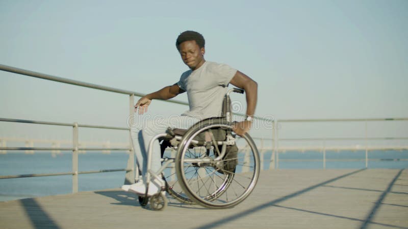 Feliz negro en silla de ruedas divirtiéndose en el paseo marítimo. metrajes