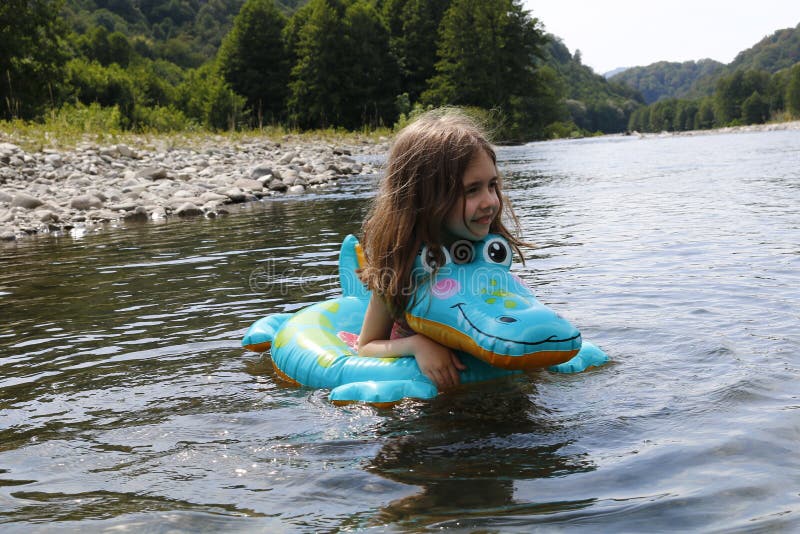 Feliz niña risible disfrutando nadando en el río con cocodrilo de anillo de goma fotografía de archivo