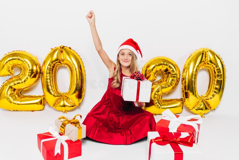 Feliz niñita en Santa hat, un bebé elegante se alegra de un regalo de Navidad mostrando gesto de victoria mientras se sienta de foto de archivo libre de regalías Feliz niñita en Santa hat, un bebé elegante se alegra de un regalo de Navidad mostrando gesto de victoria mientras se sienta de foto de archivo libre de regalías