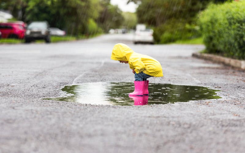 Feliz niño gracioso con impermeable bajo el día de lluvia de verano fotos de archivo