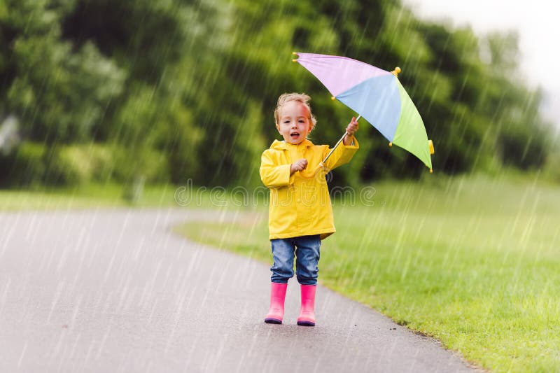 Feliz niño gracioso con paraguas multicolor bajo el día de lluvia de verano fotos de archivo