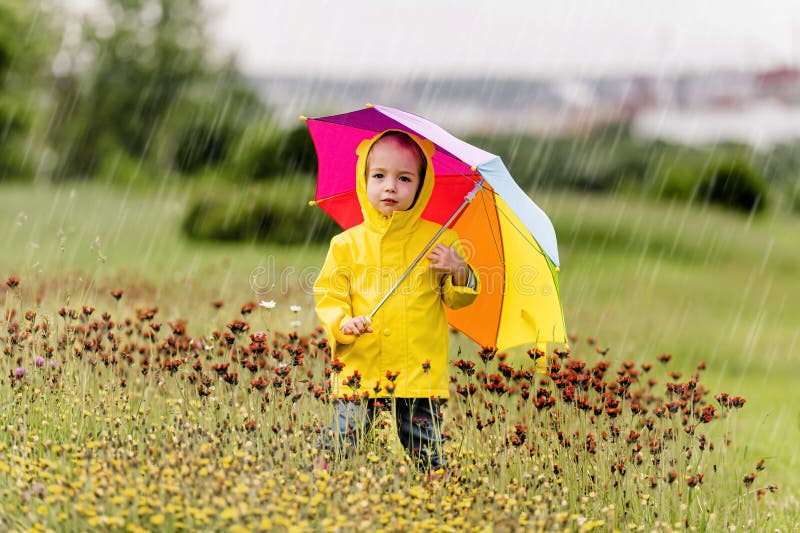Feliz niño gracioso con paraguas multicolor bajo el día de lluvia de verano imagenes de archivo