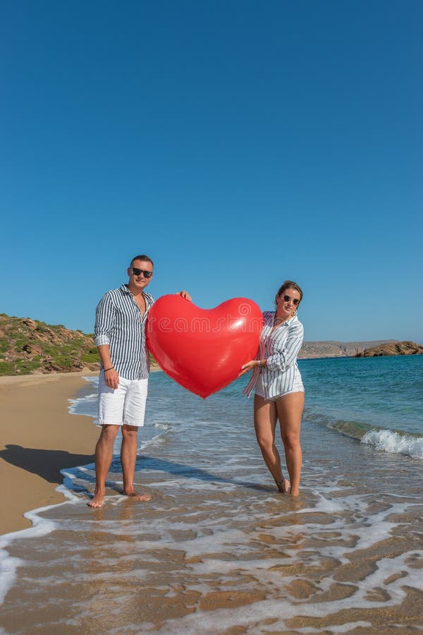 Feliz pareja amorosa en la playa con un gran globo de corazón Concepto de amor de verano imagen de archivo Feliz pareja amorosa en la playa con un gran globo de corazón Concepto de amor de verano imagen de archivo