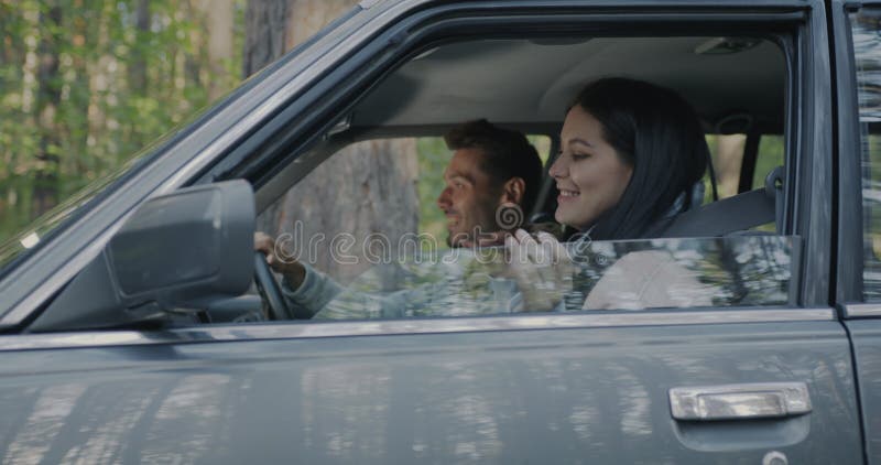 Feliz pareja joven empezando un viaje por carretera cantando sentado en un coche con el bosque verde como fondo