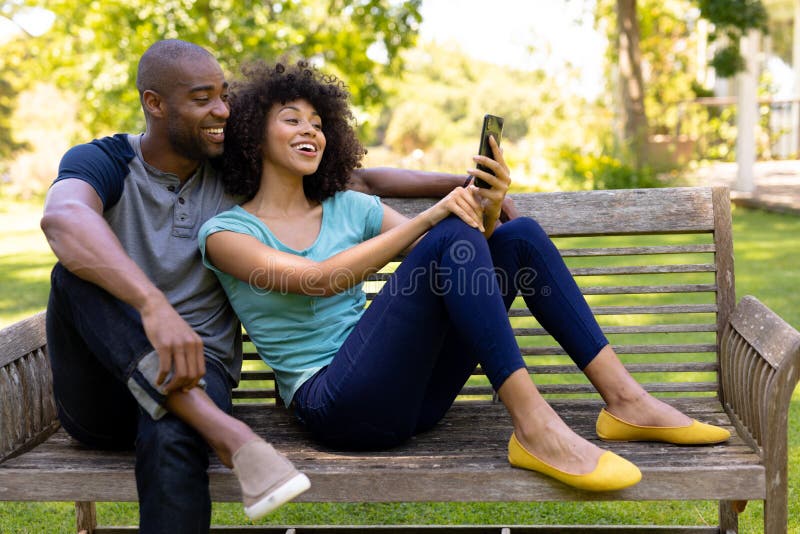 Feliz pareja joven sentada en un banco en el jardín imagen de archivo libre de regalías Feliz pareja joven sentada en un banco en el jardín imagen de archivo libre de regalías