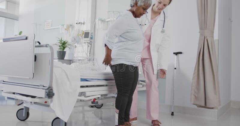 Feliz y diversa doctora que ayuda a pacientes de edad avanzada a pararse desde el espacio de copia en cámara lenta de la cama almacen de metraje de vídeo