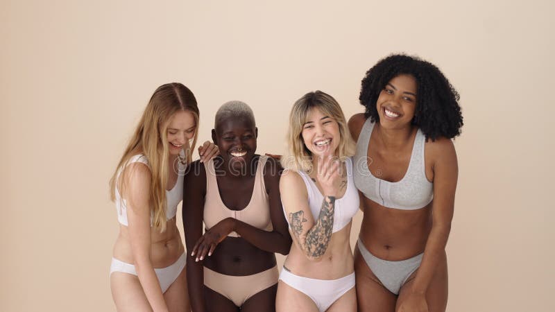 Feliz y diversa mujer con ropa interior riéndose con fondo beige.