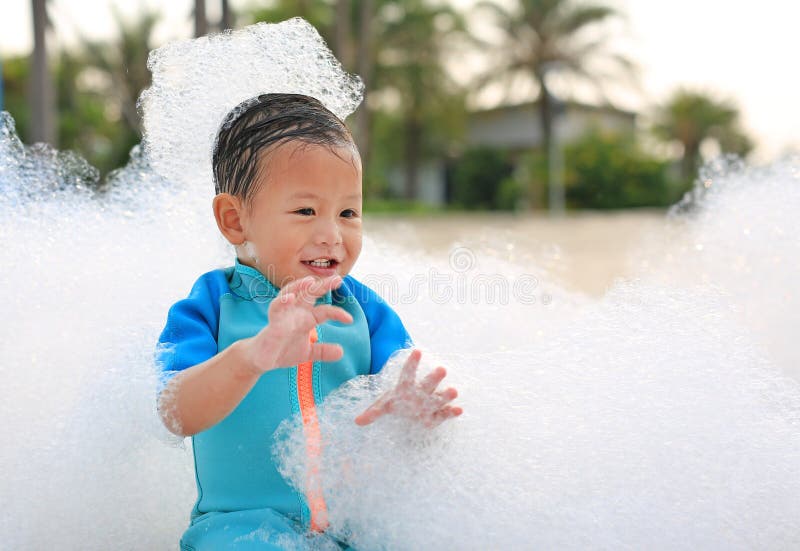 Feliz y diversión del niño pequeño asiático con traje de baño divirtiéndose en una fiesta de espuma en la piscina al aire libre imagenes de archivo