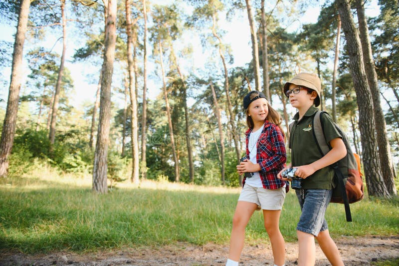 Feliz y emocionado colegio niños con mochilas con ropa informal disfrutando de caminar en el bosque el soleado día de otoño dos ac imagenes de archivo