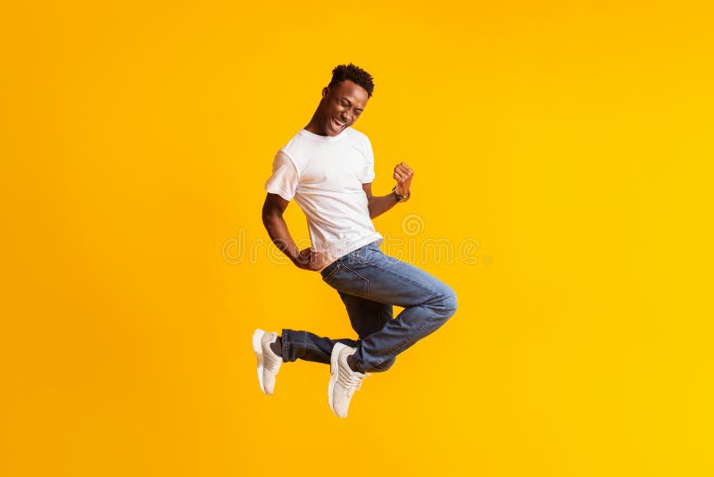 Feliz y emocionado joven negro saltando sobre amarillo imagenes de archivo