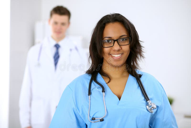 Female african american medical doctor with colleagues in background at hospital. Medicine and health care concept stock image Female african american medical doctor with colleagues in background at hospital. Medicine and health care concept stock image