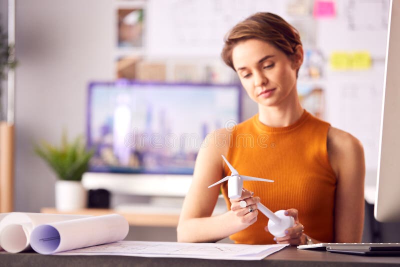 Female Architect In Office Working On Drawings For Renewable Energy Project With Model Wind Turbine royalty free stock photography