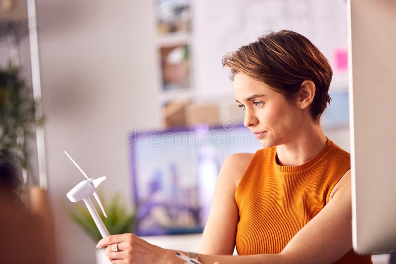 Female Architect In Office Working On Drawings For Renewable Energy Project With Model Wind Turbine royalty free stock photo
