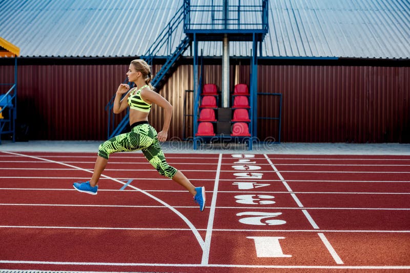 Young, beautiful girl athlete in sportswear runs along the treadmill. Sport background. Outdoor stadium. Young, beautiful girl athlete in sportswear runs along the treadmill. Sport background. Outdoor stadium