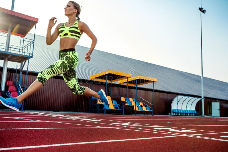 Young, beautiful girl athlete in sportswear runs along the treadmill. Sport background. Outdoor stadium. Young, beautiful girl athlete in sportswear runs along the treadmill. Sport background. Outdoor stadium