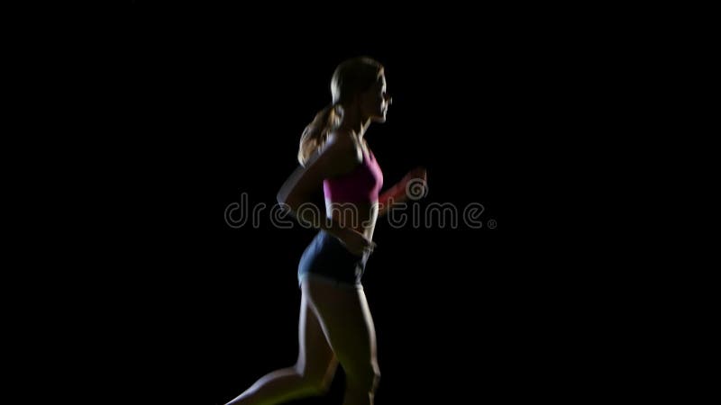 Female athlete runs beautifully in a half turn on a black background. Silhouette