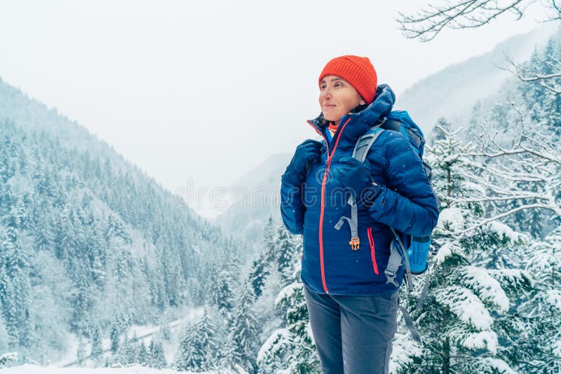 Žena batohom s batohom oblečená teplá páperová bunda si užíva zasneženú horskú krajinu, zatiaľ čo ona chodí na zimné hory