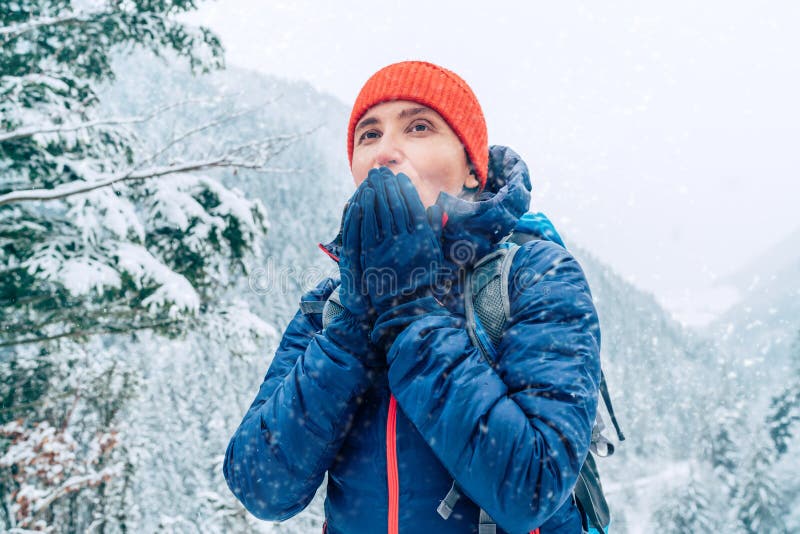 Žena Backpacker s batohom oblečená teplá páperová bunda otepľovanie dlane ruky a teší zasnežené hory krajiny, zatiaľ čo ona