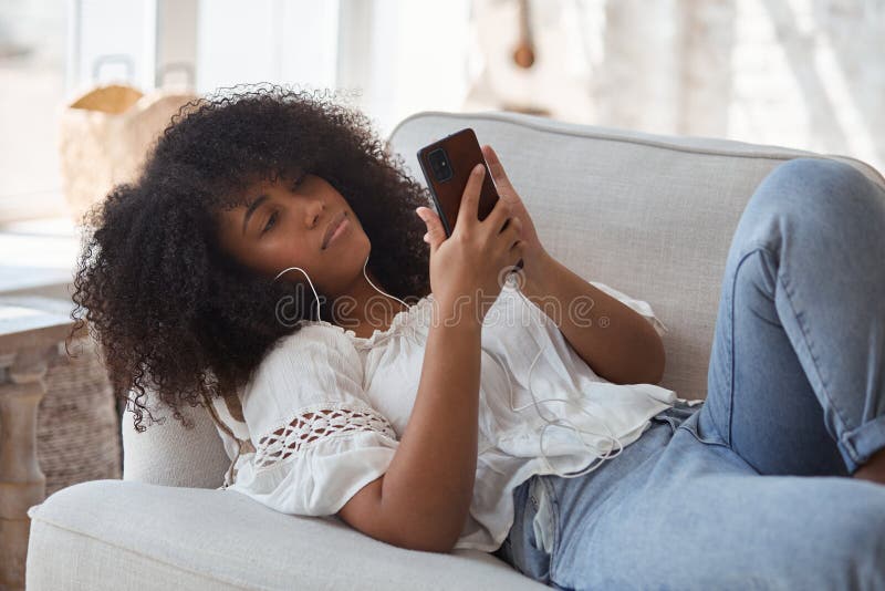 Female black student sitting on sofa and making video call.