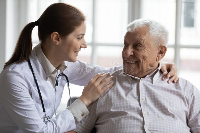 Female caregiver doctor supporting smiling older man, touching shoulders, young woman therapist gp comforting mature senior patient, having pleasant conversation, warm relationship, healthcare