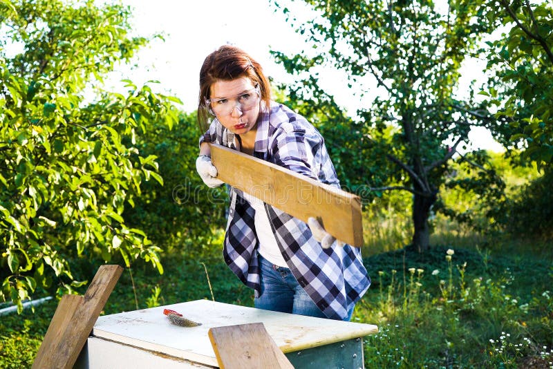 Female carpenter in protective glasses blowing off dust from wooden plank royalty free stock photo Female carpenter in protective glasses blowing off dust from wooden plank royalty free stock photo