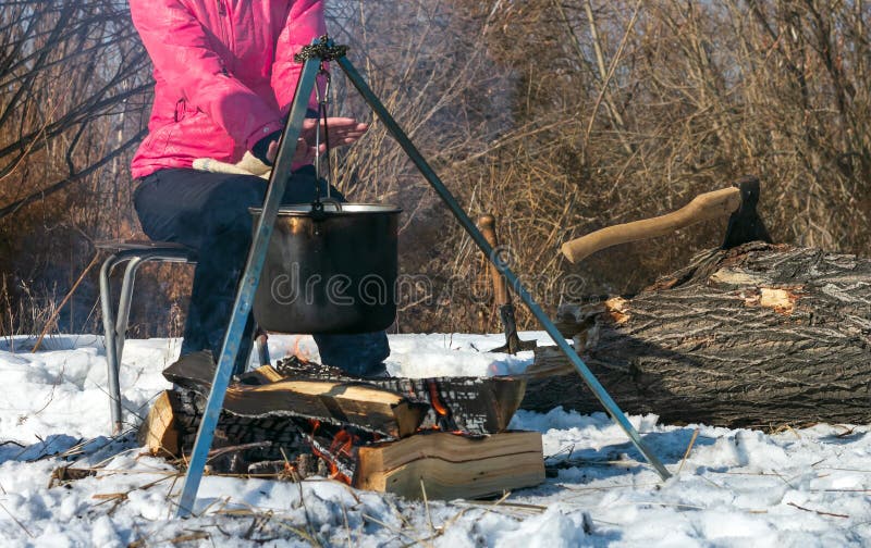 Over the fire hangs a pot in which to cook food. On a hook on a tripod,  steam comes out of the pan. Winter Camping outdoor cooking Stock Photo -  Alamy