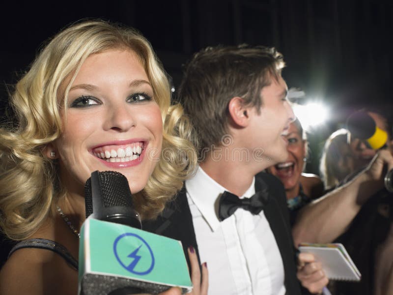 Lächelnde junge weibliche Berühmtheit sprechen in das Mikrofon mit paparazzi im hintergrund.