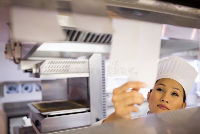 Close-up di una giovane donna chef attraversando cottura lista di controllo al contatore di cucina.