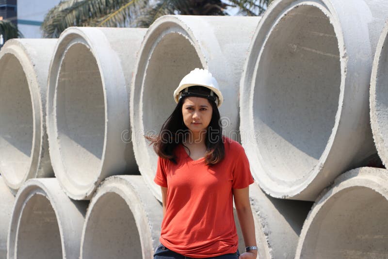 Female civil engineer or architect wear the white helmet standing on background of large cement pipes stacked. To prepare for embed into the ground as a sewer stock images Female civil engineer or architect wear the white helmet standing on background of large cement pipes stacked. To prepare for embed into the ground as a sewer stock images