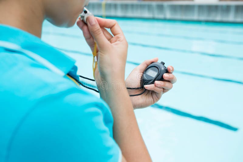 Female Coach Blowing Whistle and Looking at Stopwatch Stock Photo