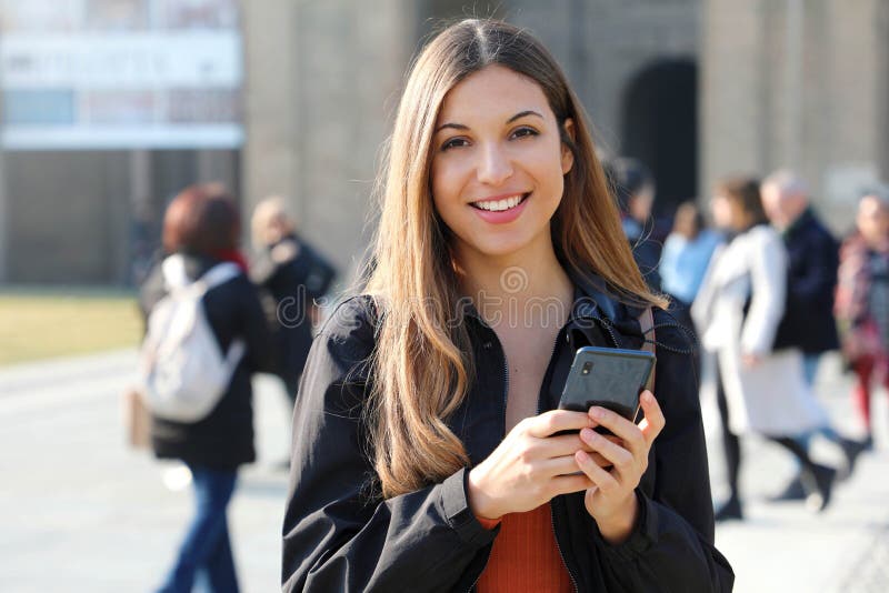 Female college student with phone outdoors. Smiling school girl with backpack standing at campus. Portrait of student outside the royalty free stock photo