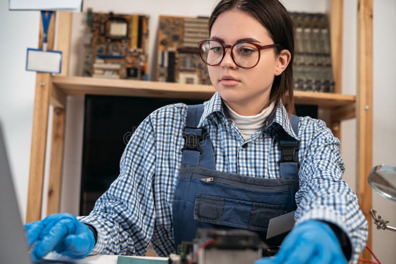 Female computer repairman working on repairing computer in IT workshop watching online courses using laptop. royalty free stock image