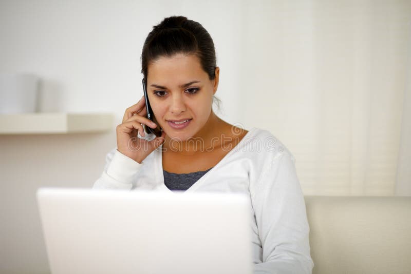 Portrait of a young female conversing on cellphone in front of her laptop computer. Portrait of a young female conversing on cellphone in front of her laptop computer