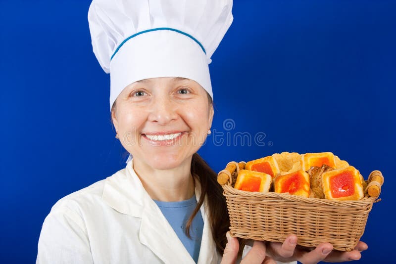 Senior cook in toque with pastry over blue background. Senior cook in toque with pastry over blue background