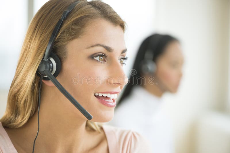 Happy female customer service representative looking away with colleague in background