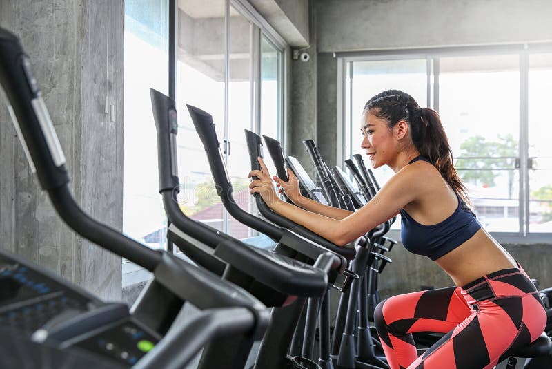 The female is cycling in the gym. Portrait of girl exercising on cardio machines in the sport club. Pretty women body builder stock photos The female is cycling in the gym. Portrait of girl exercising on cardio machines in the sport club. Pretty women body builder stock photos