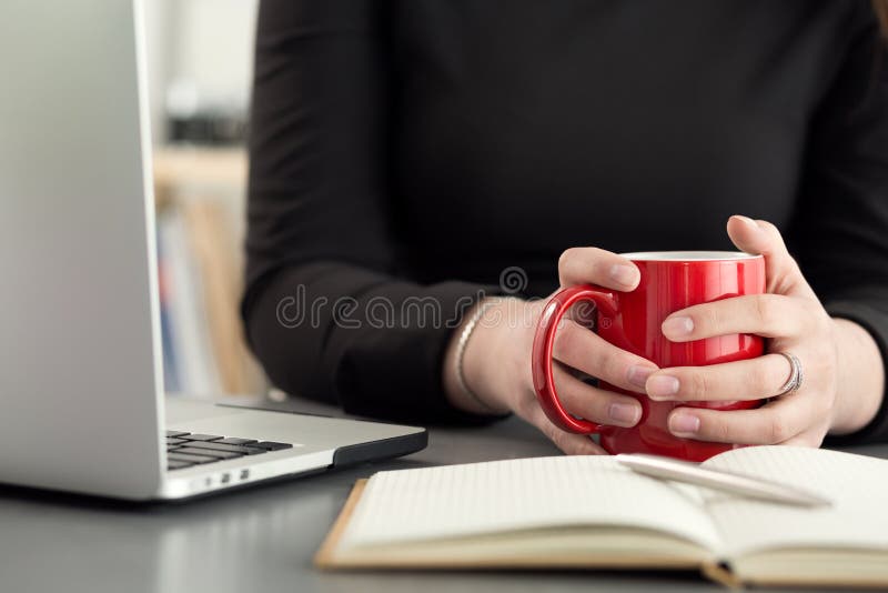 Female designers in office drinking morning tea or coffee. Coffeebreak during hard working day. Girl holding cup of hot beverage.