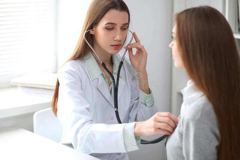 Female doctor examining her patient with stethoscope while sitting at the table near the window in hospital. Physician stock photos Female doctor examining her patient with stethoscope while sitting at the table near the window in hospital. Physician stock photos