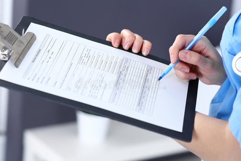 Female doctor filling up medical form on clipboard, closeup. Physician finishing up examining his patient in hospita