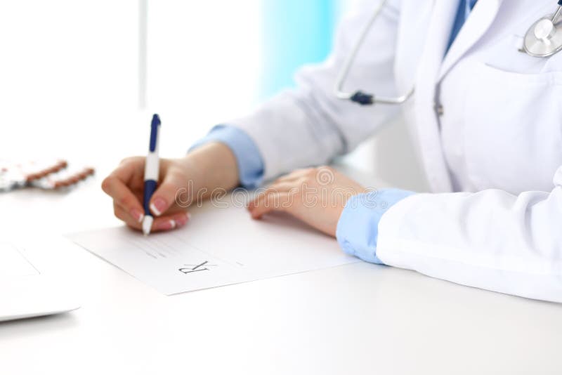 Female doctor filling up prescription form while sitting at the desk in hospital closeup. Physician finishing u