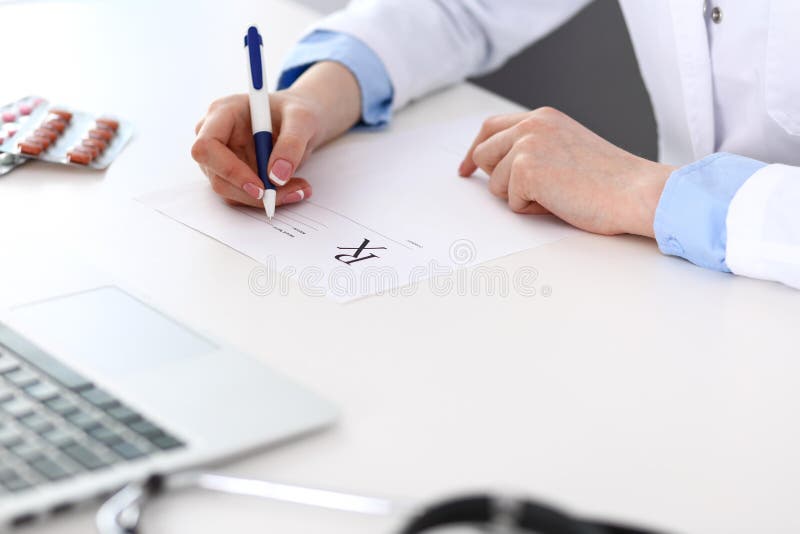 Female doctor filling up prescription form while sitting at the desk in hospital closeup. Physician finishing u