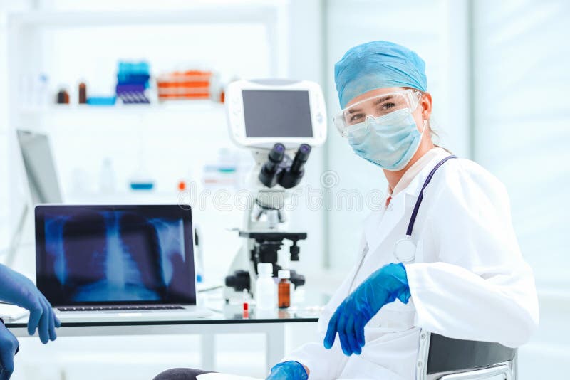 Female doctor in a protective mask sitting at a laboratory table.