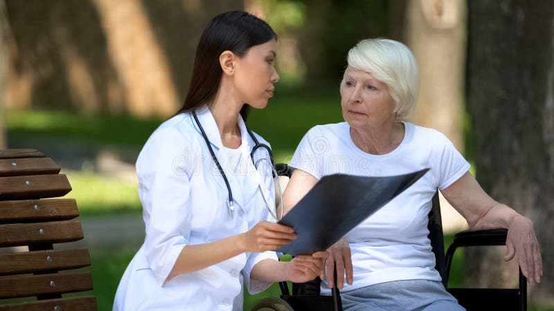 Female doctor showing spinal x-ray result to disabled elderly woman, day in park stock photography Female doctor showing spinal x-ray result to disabled elderly woman, day in park stock photography