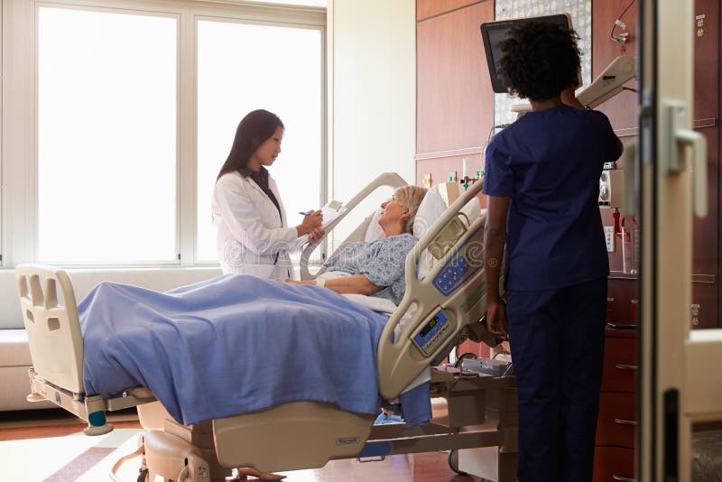 Female Doctor Talks To Senior Female Patient In Hospital Bed