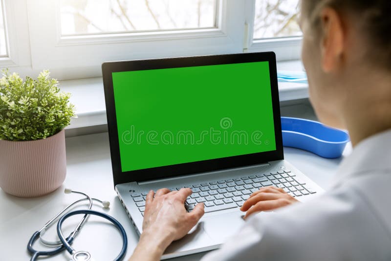 doctor typing on her laptop computer in medical clinic office. blank green screen mockup