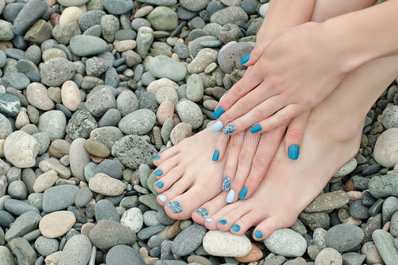 Female Feet and Hands with a Blue Manicure on Pebbles Stock Image