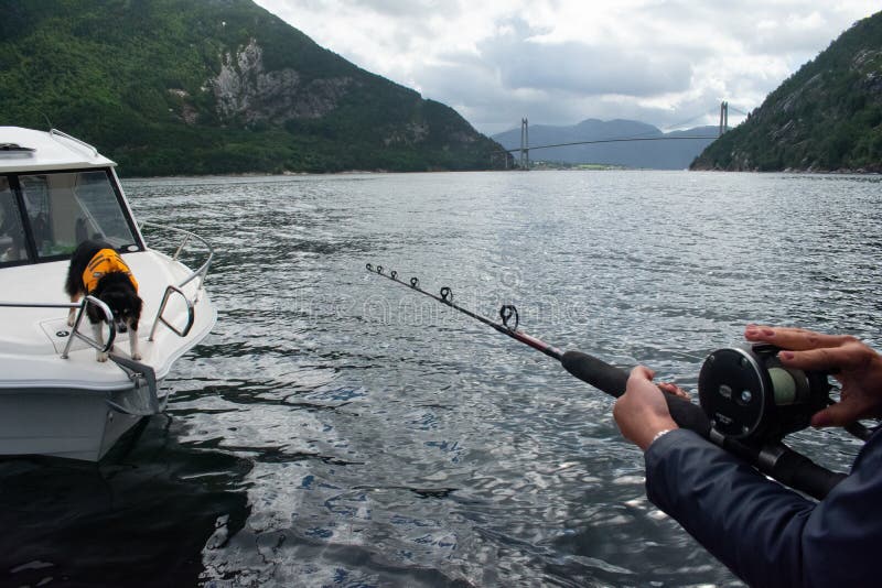 Female Fishing offshore on a boat with fishing rod and reel with mountains and fjords in background s