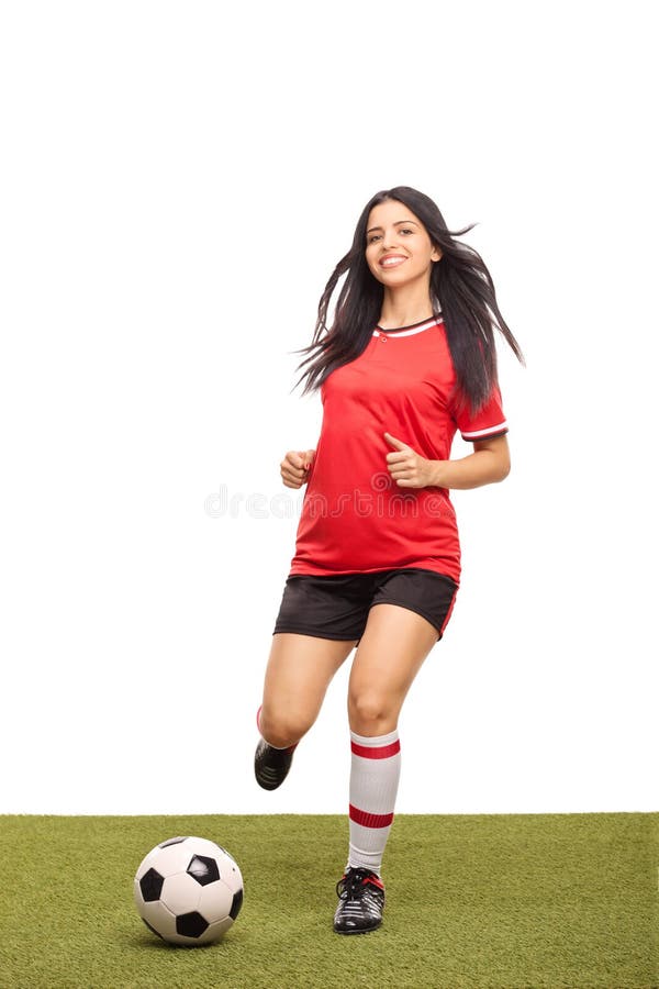 Full length portrait of a female football player kicking a ball on a grass field and looking at the camera isolated on white background. Full length portrait of a female football player kicking a ball on a grass field and looking at the camera isolated on white background