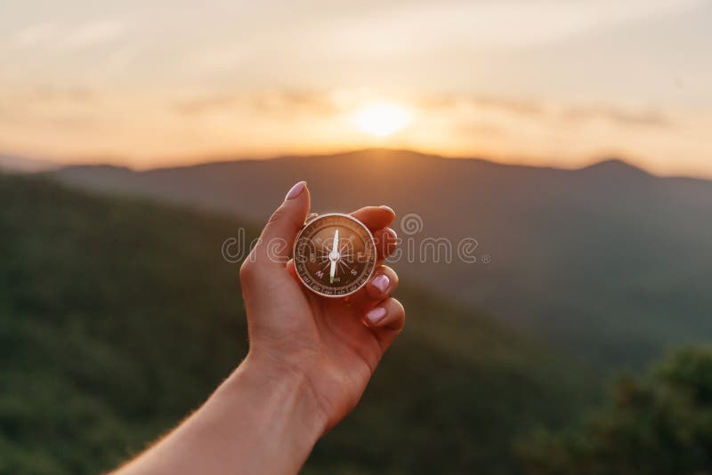 Female hand with compass in mountains at sunrise, pov.